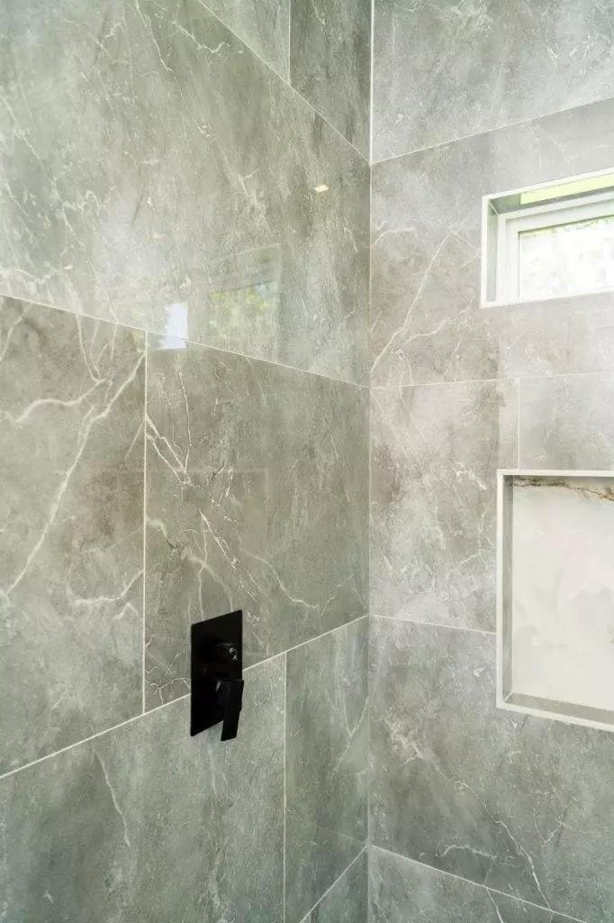 Sleek and sophisticated shower with large format polish stone gray tiles and black accessories that create a bold and modern statement Sleek and sophisticated shower with large format polish stone gray tiles and black accessories that create a bold and modern statement